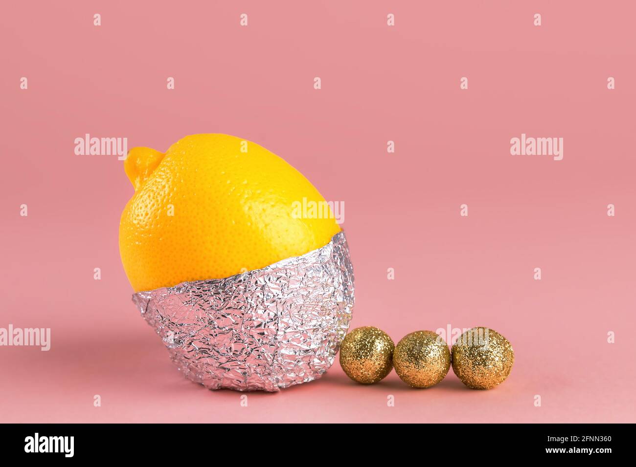 Limone fresco in lamina di alluminio e con palline dorate intorno, su sfondo rosa. Idee per feste di compleanno. Foto Stock