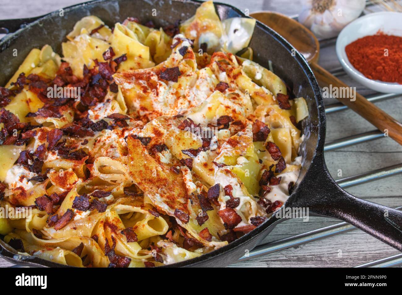 Piatto di pasta ungherese rustico Turos csuza con formaggio casereccia, quark e pancetta servita in una padella di ghisa su un tavolo Foto Stock