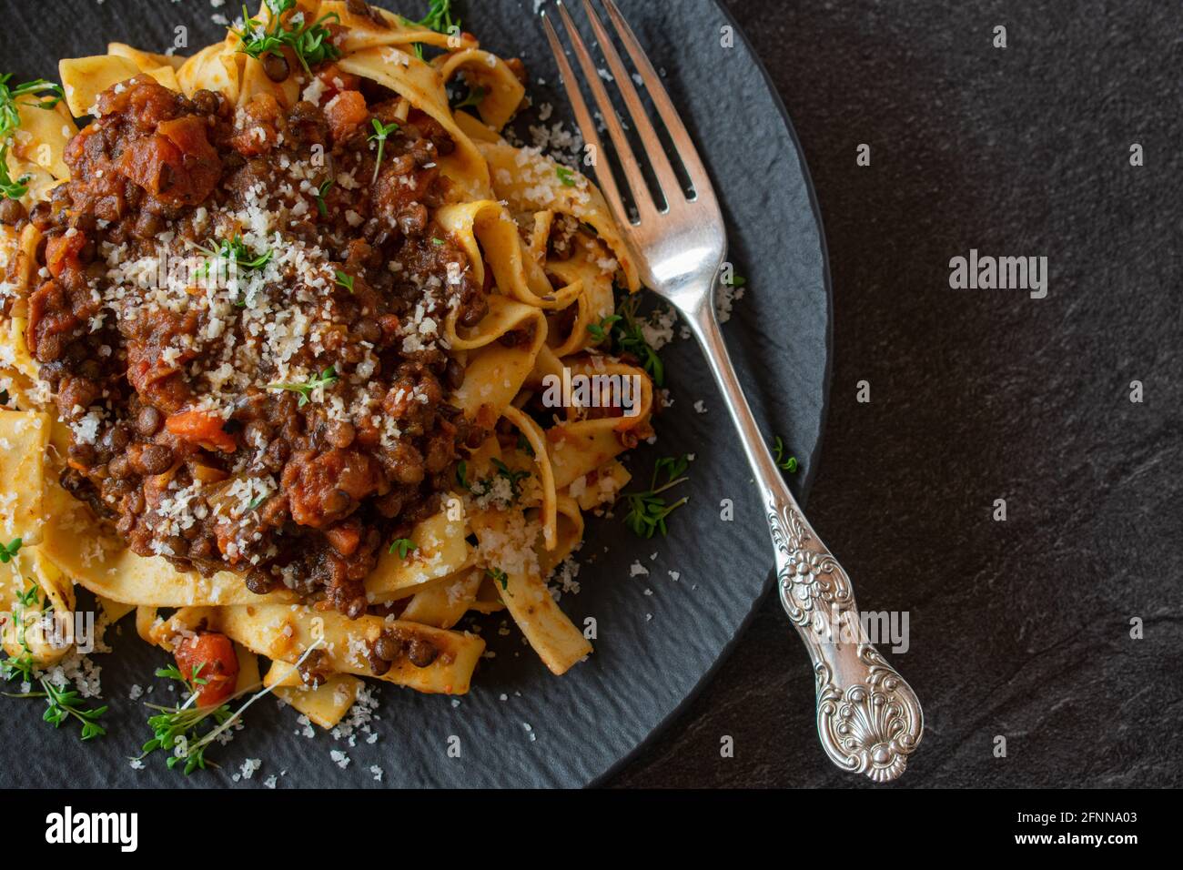 lenticchie bollognese fresche e cucinate in casa con pasta servita su piatto scuro con forchetta rustica su sfondo scuro con spazio per la copia, Foto Stock