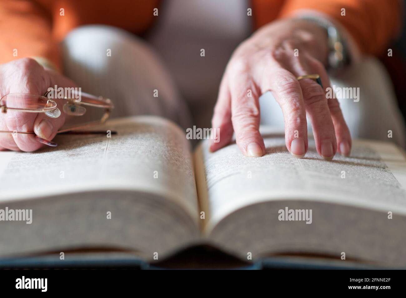 Donna anziana che legge un libro e nella sua mano tiene un paio di occhiali. Foto Stock