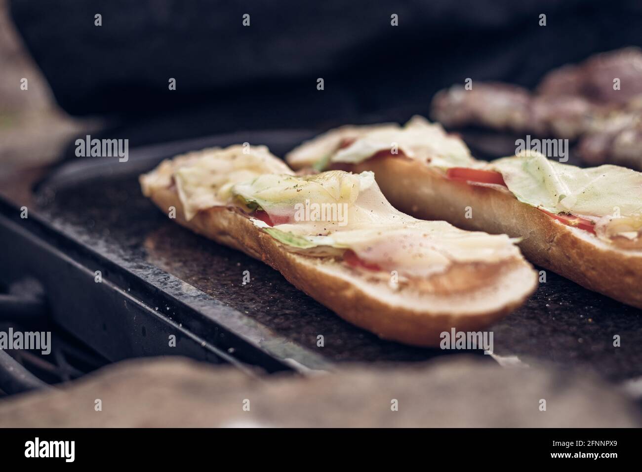 Baguette grigliate cosparse di burro e olio, prosciutto di pollo, pomodoro e ricoperte di formaggio a fette vengono cotte fino a quando non diventano dorate su una pietra di granito Foto Stock