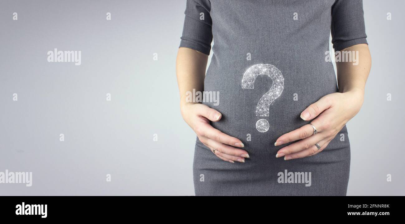 Giovane donna che tiene il ventre incinta in mani con punto interrogativo ologramma. Gravidanza, concetto di maternità. Foto Stock