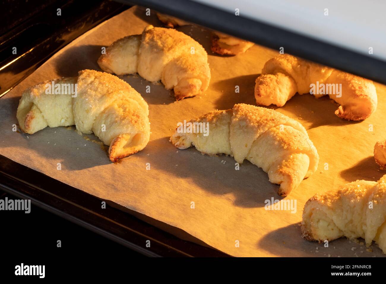 Croissant ghiacciati al forno su una teglia ricoperta di carta pergamena. Bagel dolci da un impasto di formaggio cotto in un forno caldo. Il Foto Stock