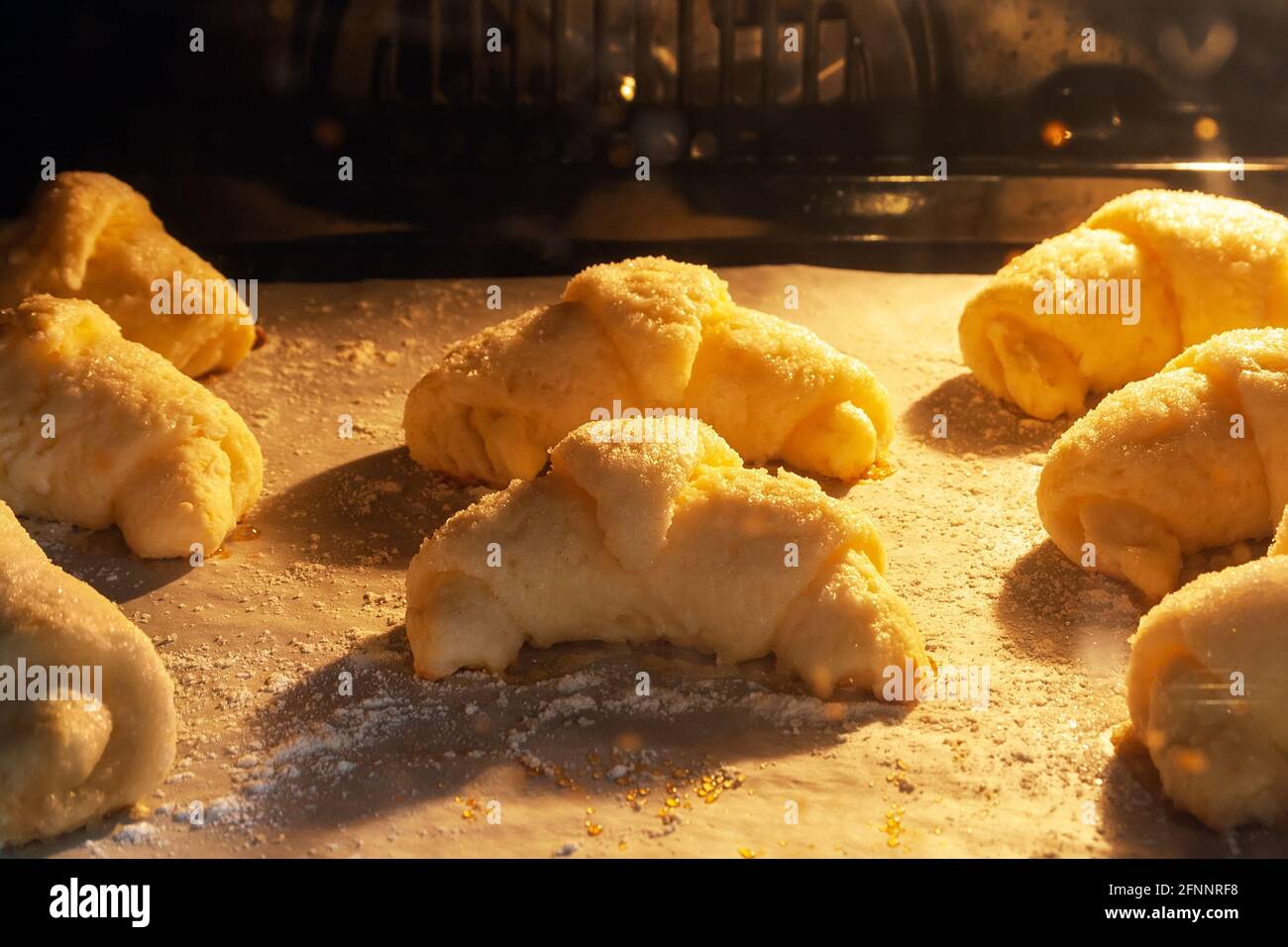 Vista a chiocciotto di croissant ghiacciati al forno adagiati su una teglia ricoperta di carta pergamena con farina. Bagel dolci da un impasto di cagliata Foto Stock