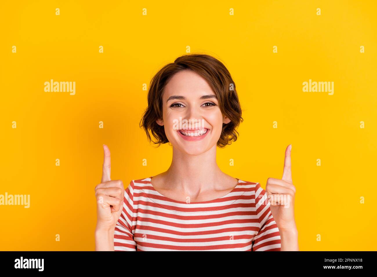 Primo piano ritratto di una bella persona sorridente che punta due dita isolato su uno sfondo di colore giallo vivace Foto Stock