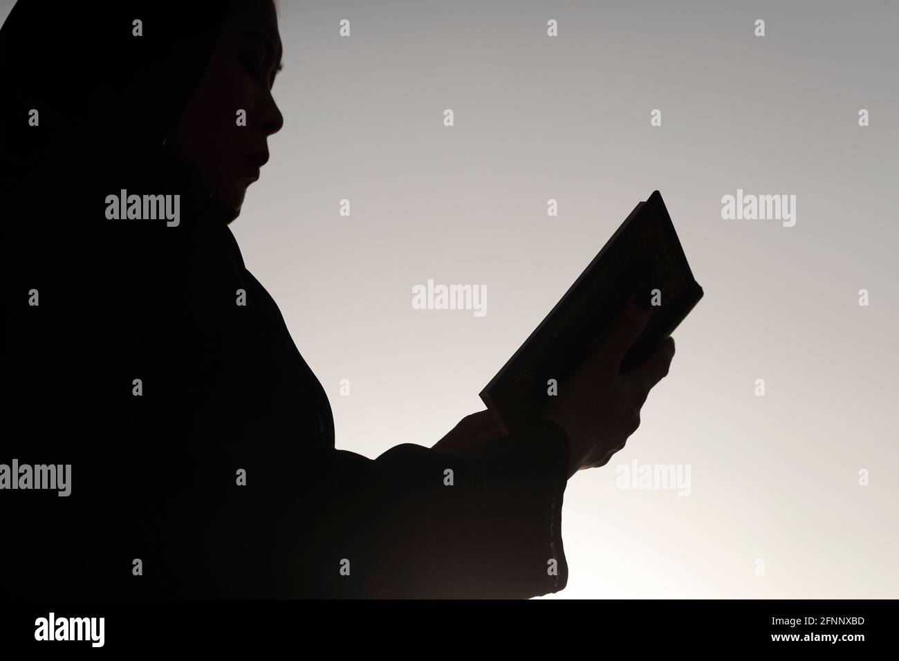 Silhouette di donna musulmana che legge il Noble Quran contro il cielo. Concetto di preghiera religiosa. Emirati Arabi Uniti Foto Stock