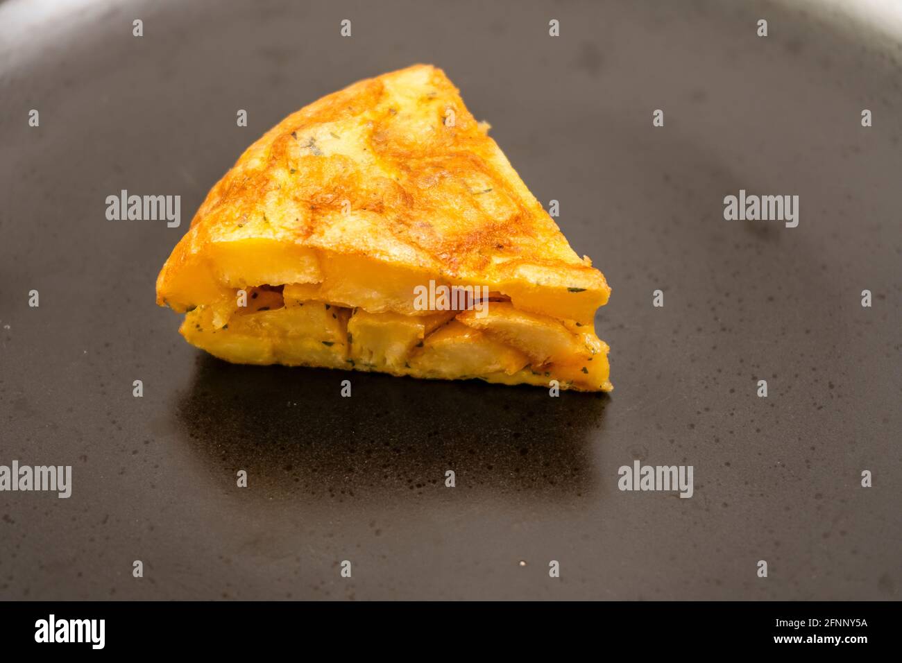 Vista ravvicinata di una porzione di omelette di patate o papà fatte in casa su un piatto nero su un tavolo di marmo chiaro. Tapas tradizionali. Foto Stock