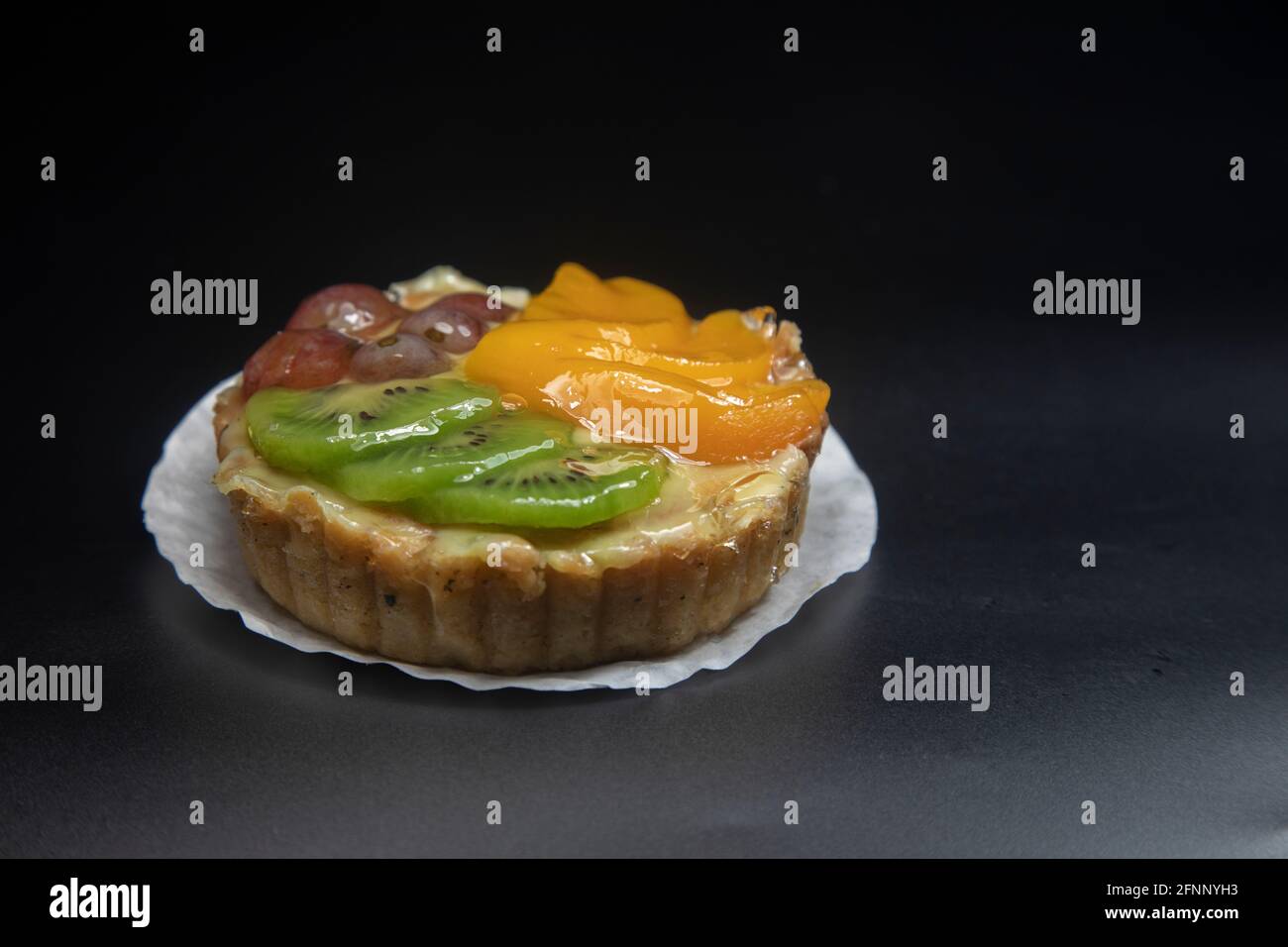 crostata di frutta accatastata con uva di pesca kiwi fondo scuro. Foto Stock