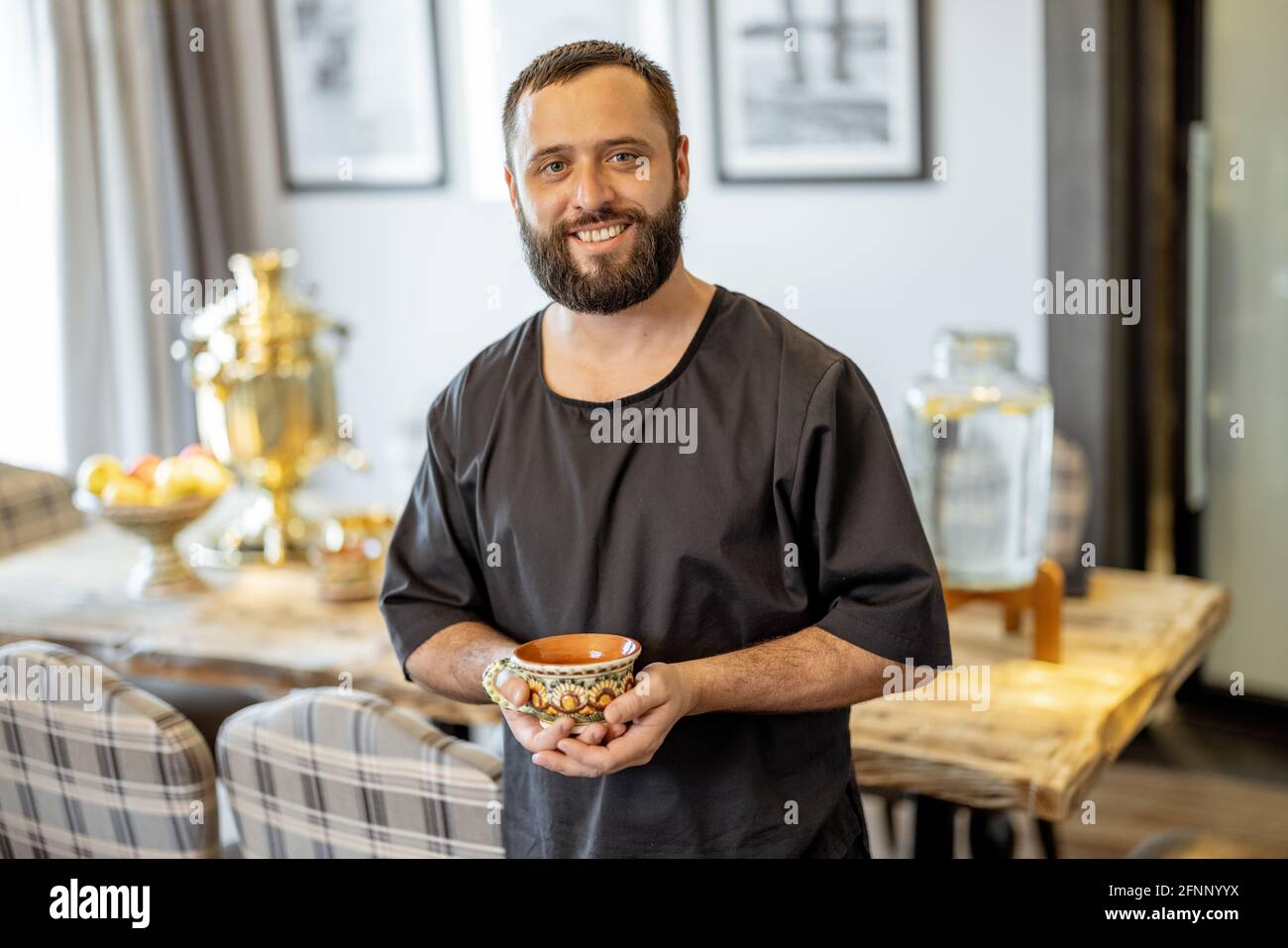 Un ritratto del bagnino che rimane prima del tavolo servito in stile russo con samovar. Uomo allegro personale in spa. Foto Stock