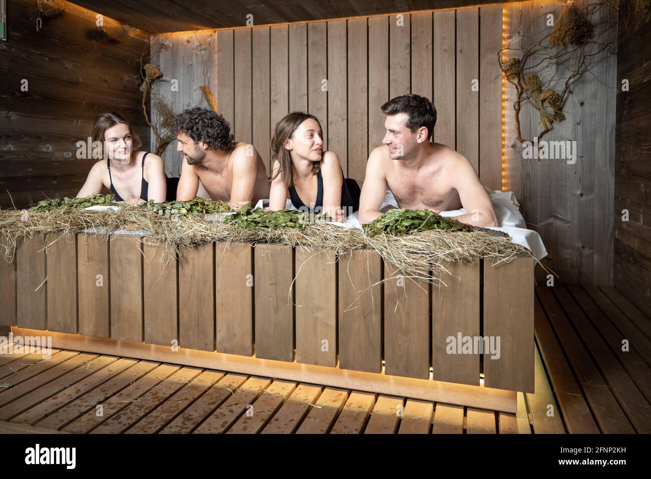 Compagnia di amici sdraiati su una panca di legno ricoperta di fieno nella sauna tradizionale russa. Benessere e svago in spa. Foto Stock