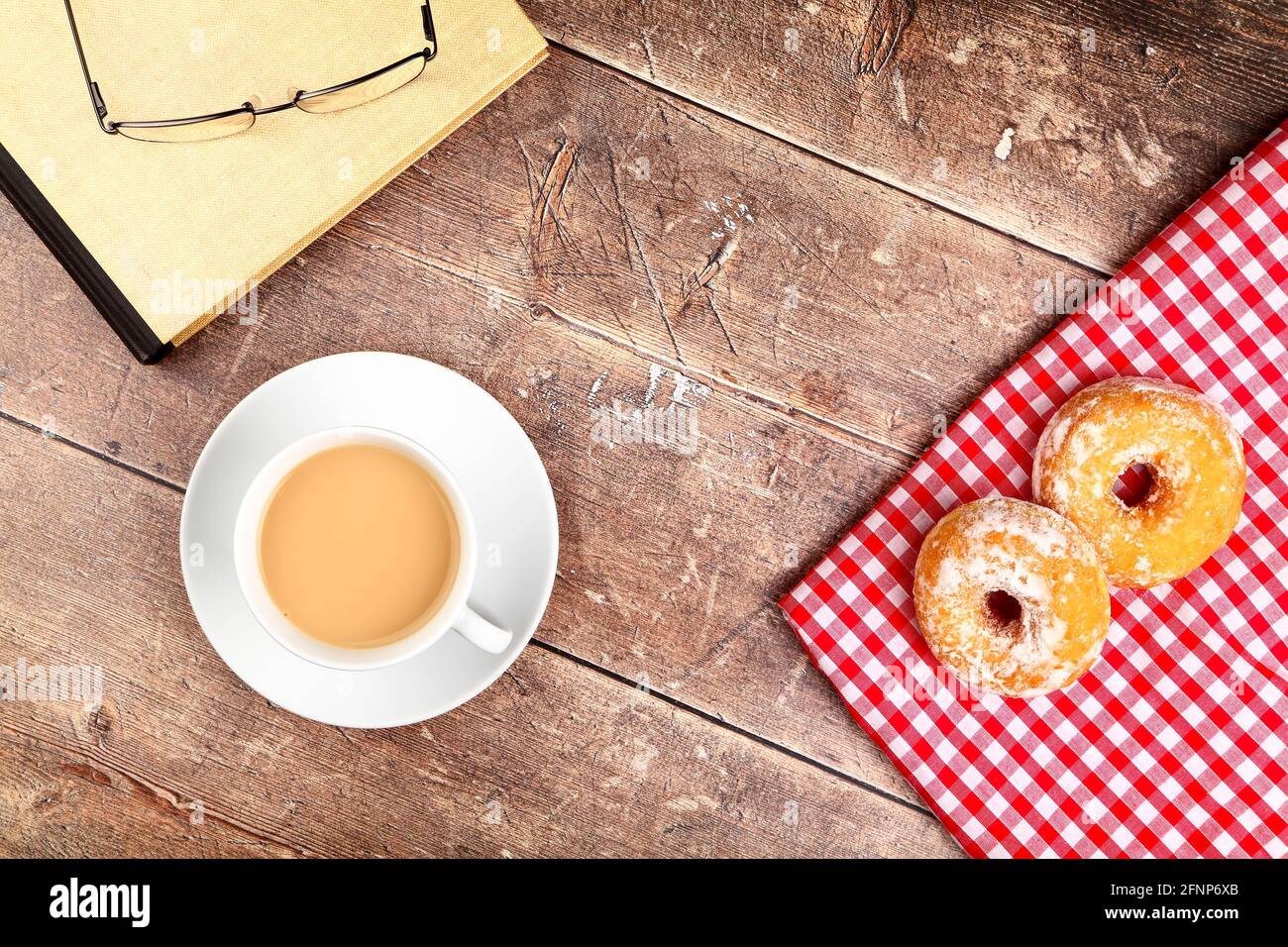 Ciambelle ad anello con una tazza di tè e una lettura libro su un tavolo di legno Foto Stock