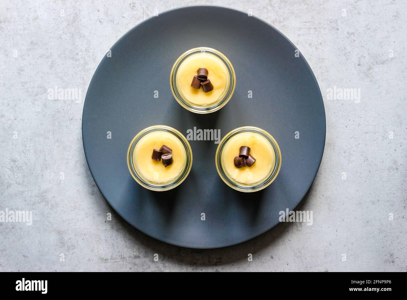 Tre bicchieri con budino alla vaniglia disposti triangolarmente su un blu piastra sparare direttamente dall'alto Foto Stock