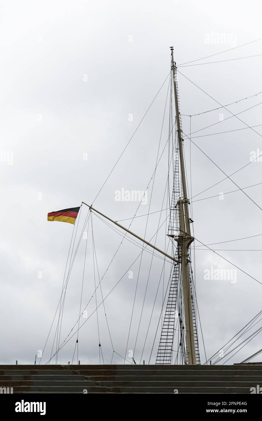 Manipolazione di una barca a vela con le torri bandiera tedesca Sopra una scala di fronte alle nuvole scure ad Amburgo Foto Stock
