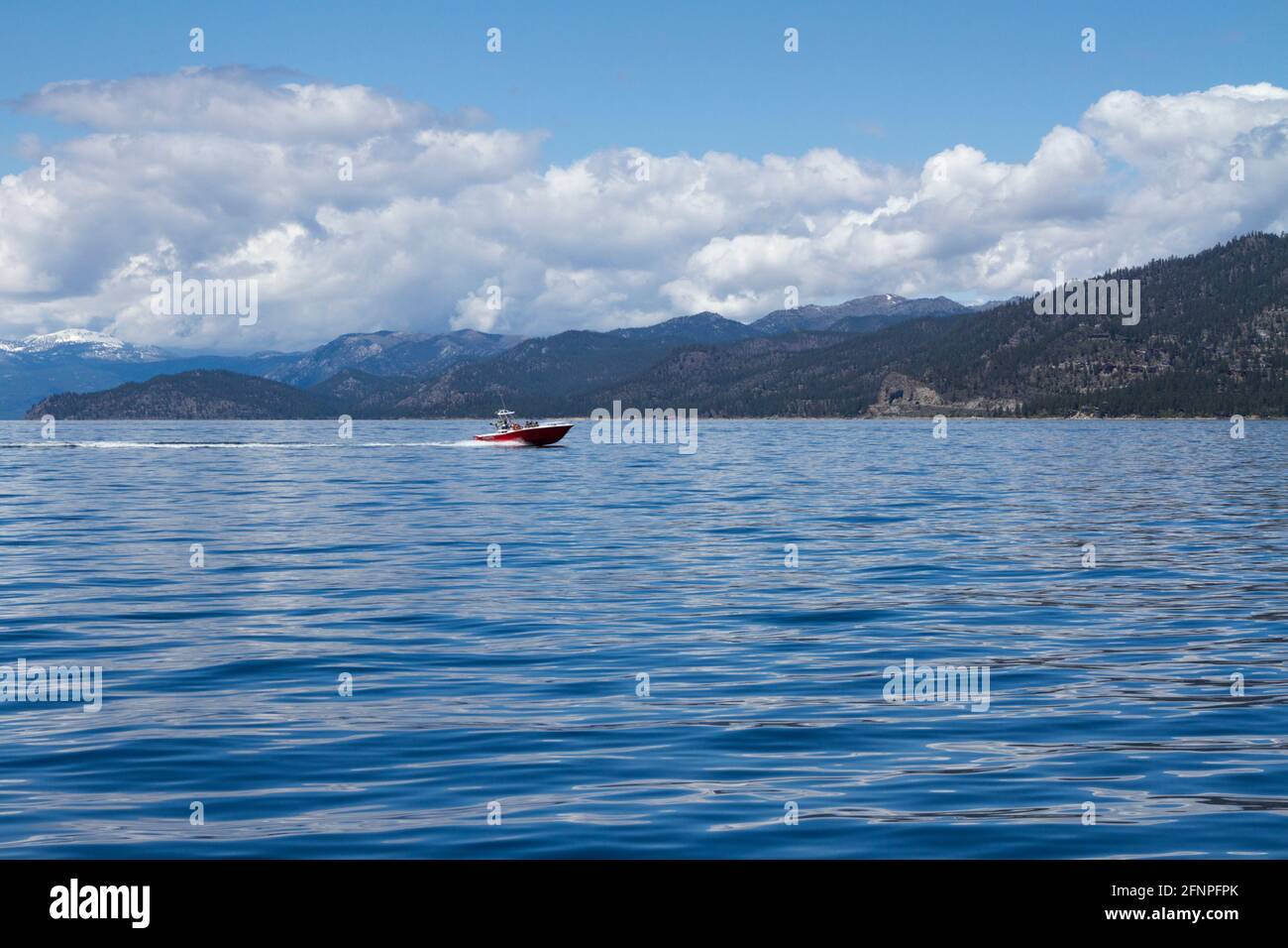 Persone che navigano su una barca rossa attraverso le acque blu di Lago Tahoe nella soleggiata giornata estiva con paesaggio verde in sfondo Foto Stock