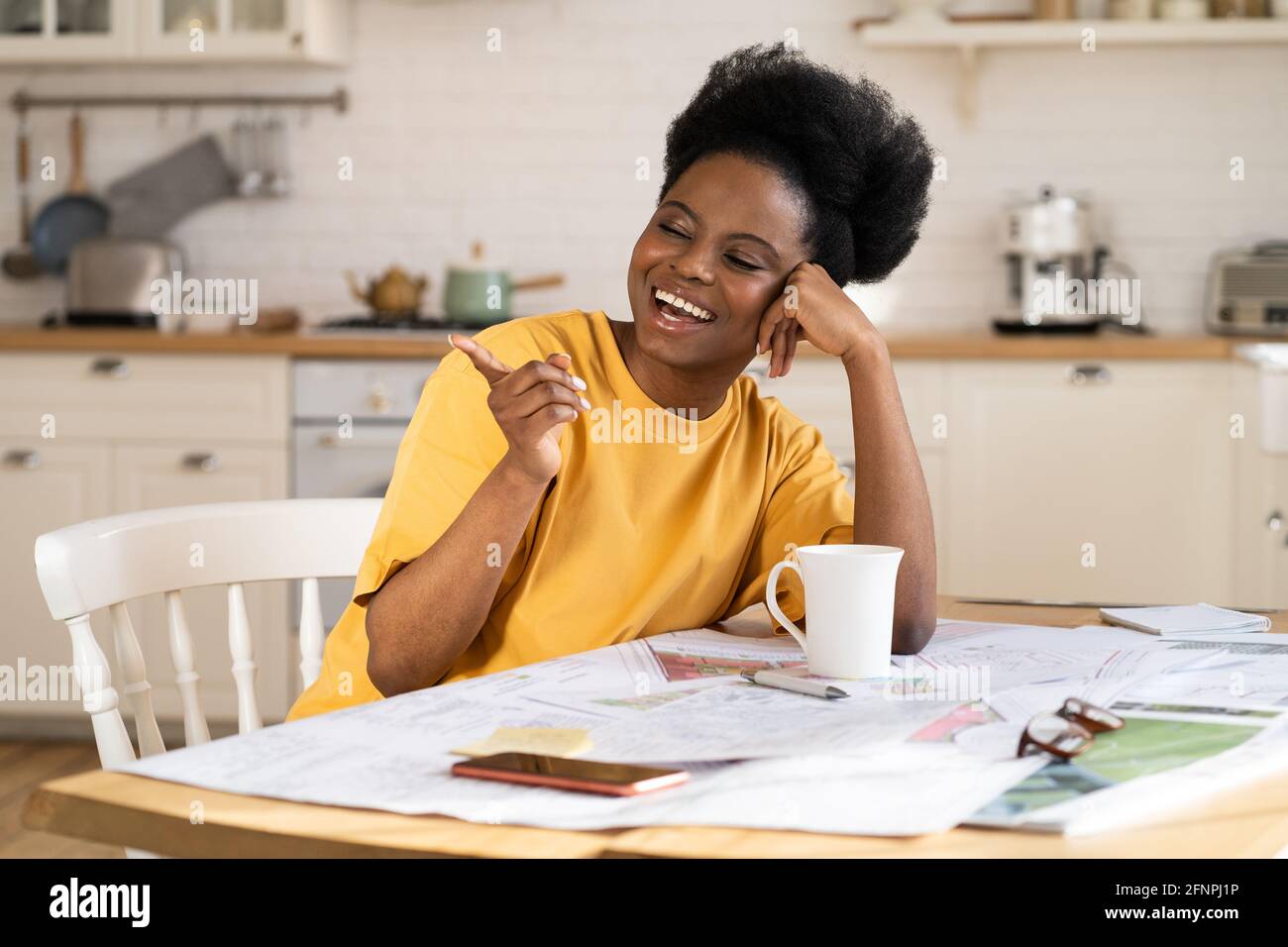 Una donna d'affari nera molto contentata ride lavoro da casa. Allegro architetto siediti a tavola con i progetti Foto Stock