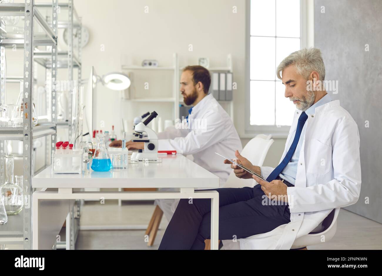 Scienziati e ricercatori seri che lavorano seduti a un tavolo dentro un laboratorio moderno Foto Stock