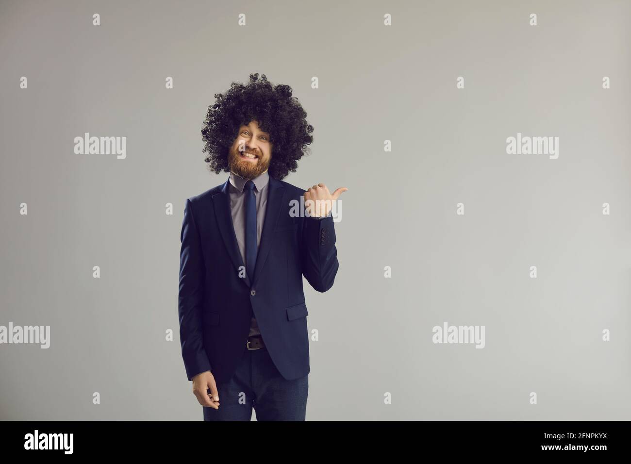 Ragazzo divertente in grande parrucca arricciata che punta il pollice via a. sfondo dello spazio di copia pubblicitario Foto Stock