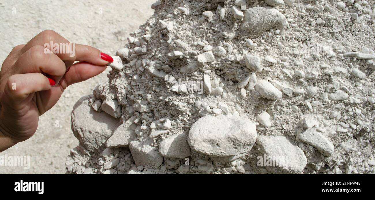Mano femminile che tiene un pezzo di gesso di una roccia bianca. Piccole pietre di calcite lisce sono mescolate con creta di gesso. Calcio in natura. Gesso bianco naturale te Foto Stock