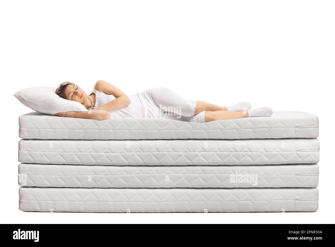 Giovane donna in pigiama dormendo su pile di materassi isolati su sfondo bianco Foto Stock