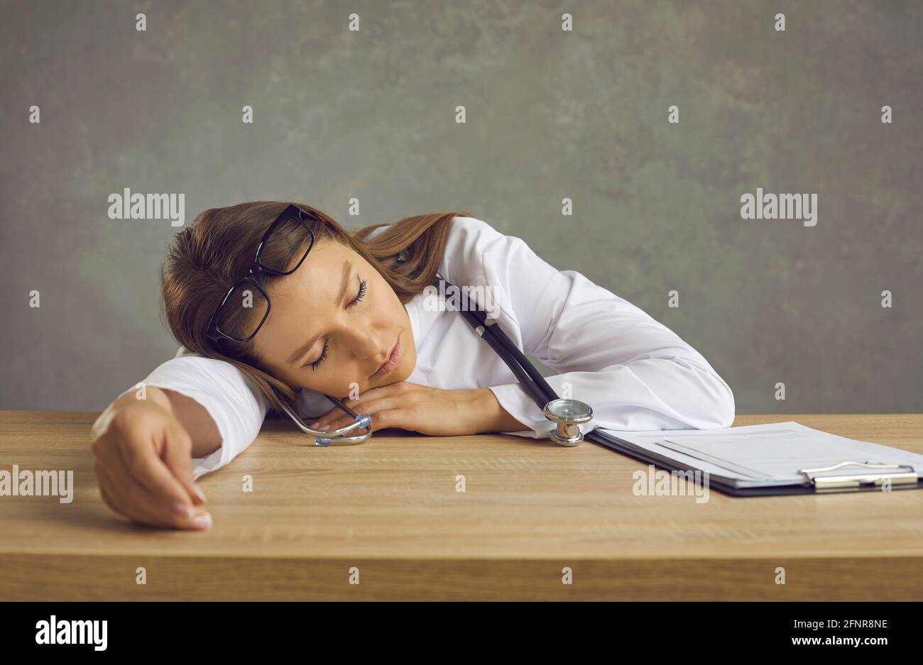 Infermiera giovane stanca o medico che dormiva seduto alla scrivania dell'ufficio dopo un lungo turno notturno Foto Stock