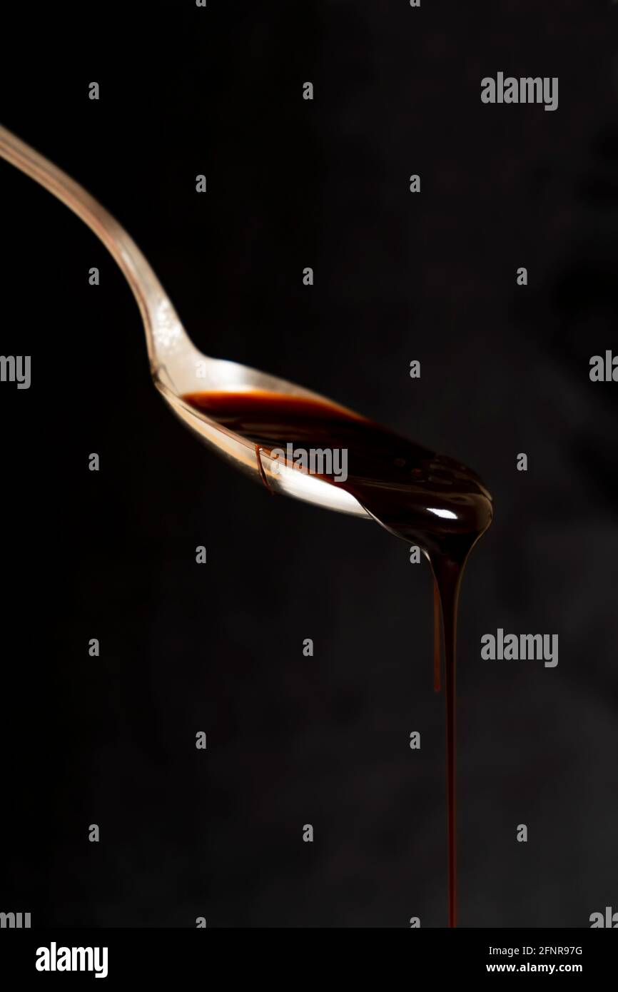 Sgocciolando il caramello da un cucchiaio su sfondo scuro. Dolcezza liquida. Foto Stock