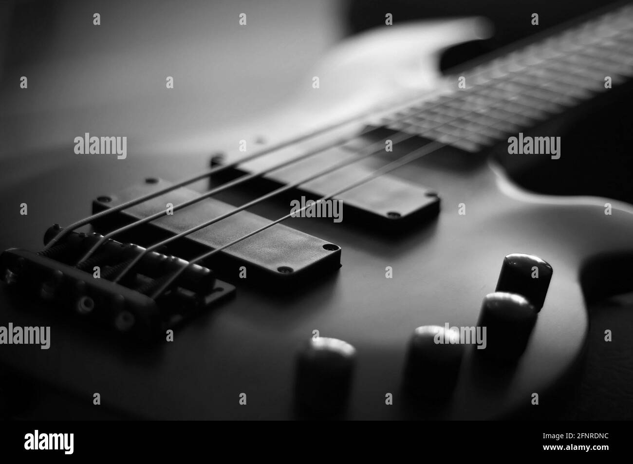 Primo piano di un corpo liscio, pickup, ponte, manopole e corde di uno strumento musicale per chitarra basso con retroilluminazione Foto Stock