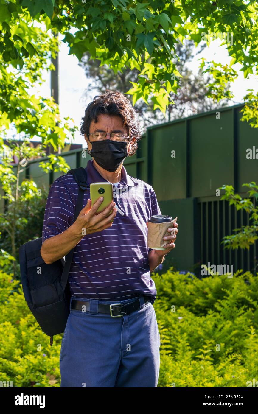 Uomo ispanico che indossa una maschera facciale su un parco che beve caffè Foto Stock