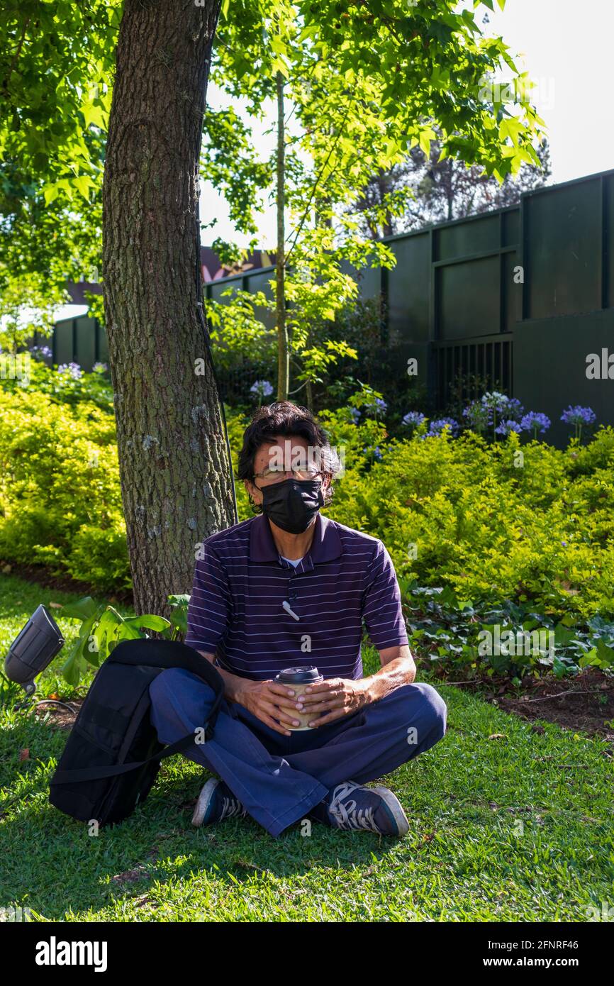 Uomo ispanico che indossa una maschera facciale su un parco che beve caffè Foto Stock