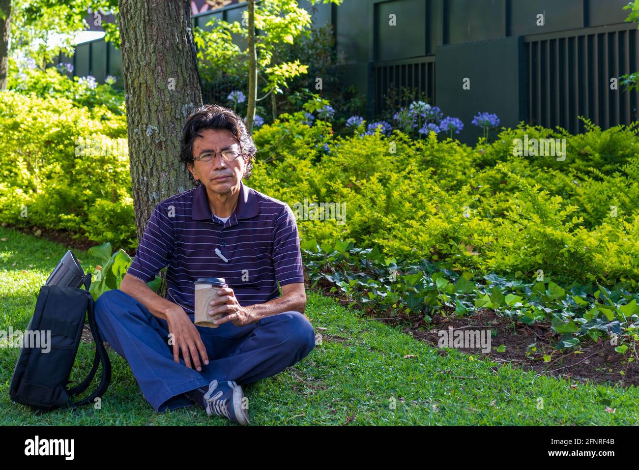 Uomo ispanico che indossa una maschera facciale su un parco che beve caffè Foto Stock