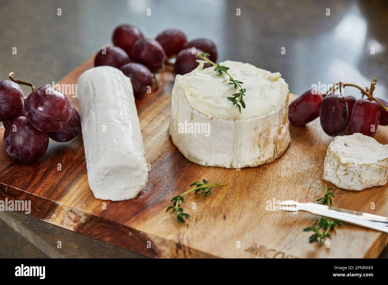 Formaggi francesi selezionati con uva, su tavola di legno con rosmarino e coltello. Foto Stock