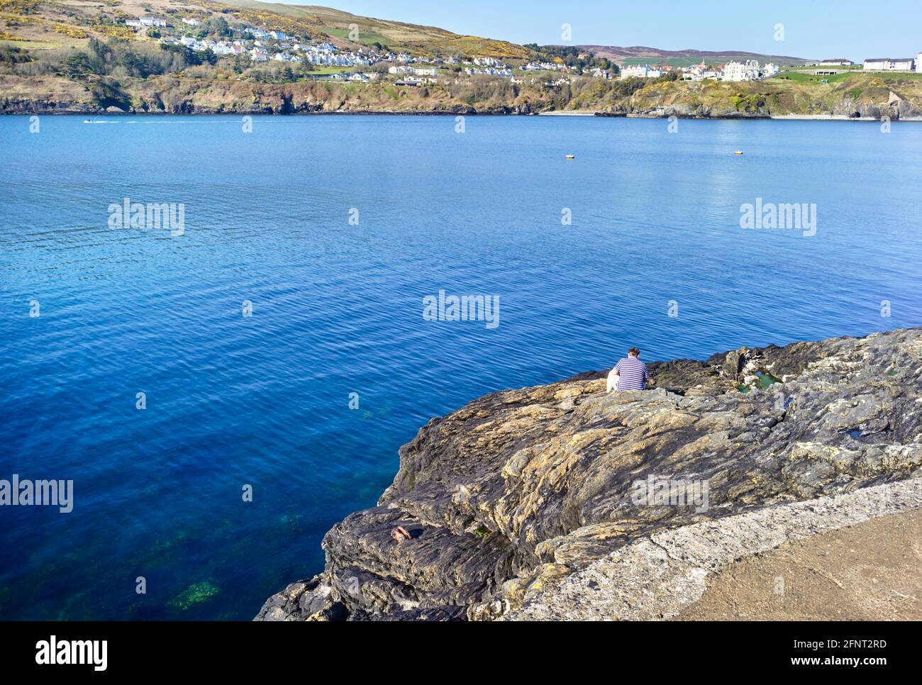 Un pescatore solista seduto su una roccia a Port Erin, Isola di Man Foto Stock