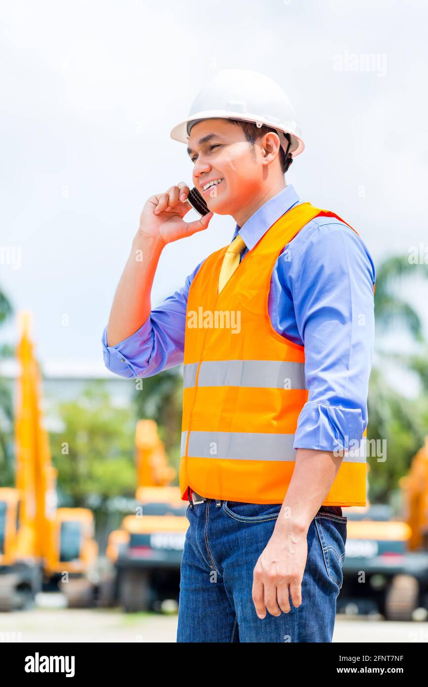 Asian foreman telefonare con il cellulare del sito di costruzione o di estrazione mineraria o società di noleggio Foto Stock