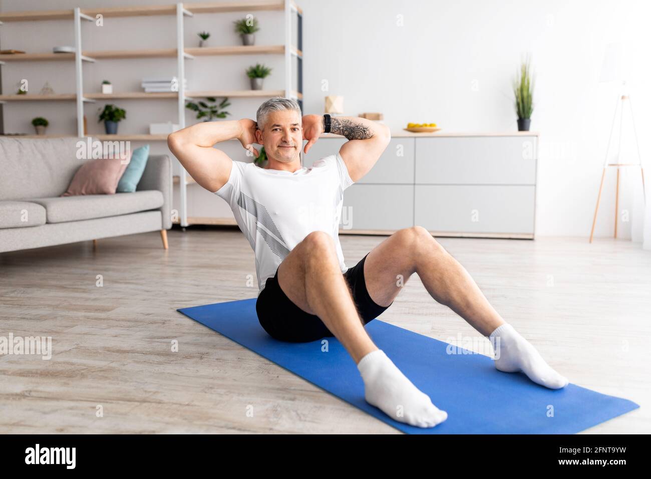 Allenamento mattutino maschile. Uomo di mezza età che fa sit-up abs esercizio su tappeto sportivo, allenamento e allenarsi in salotto Foto Stock