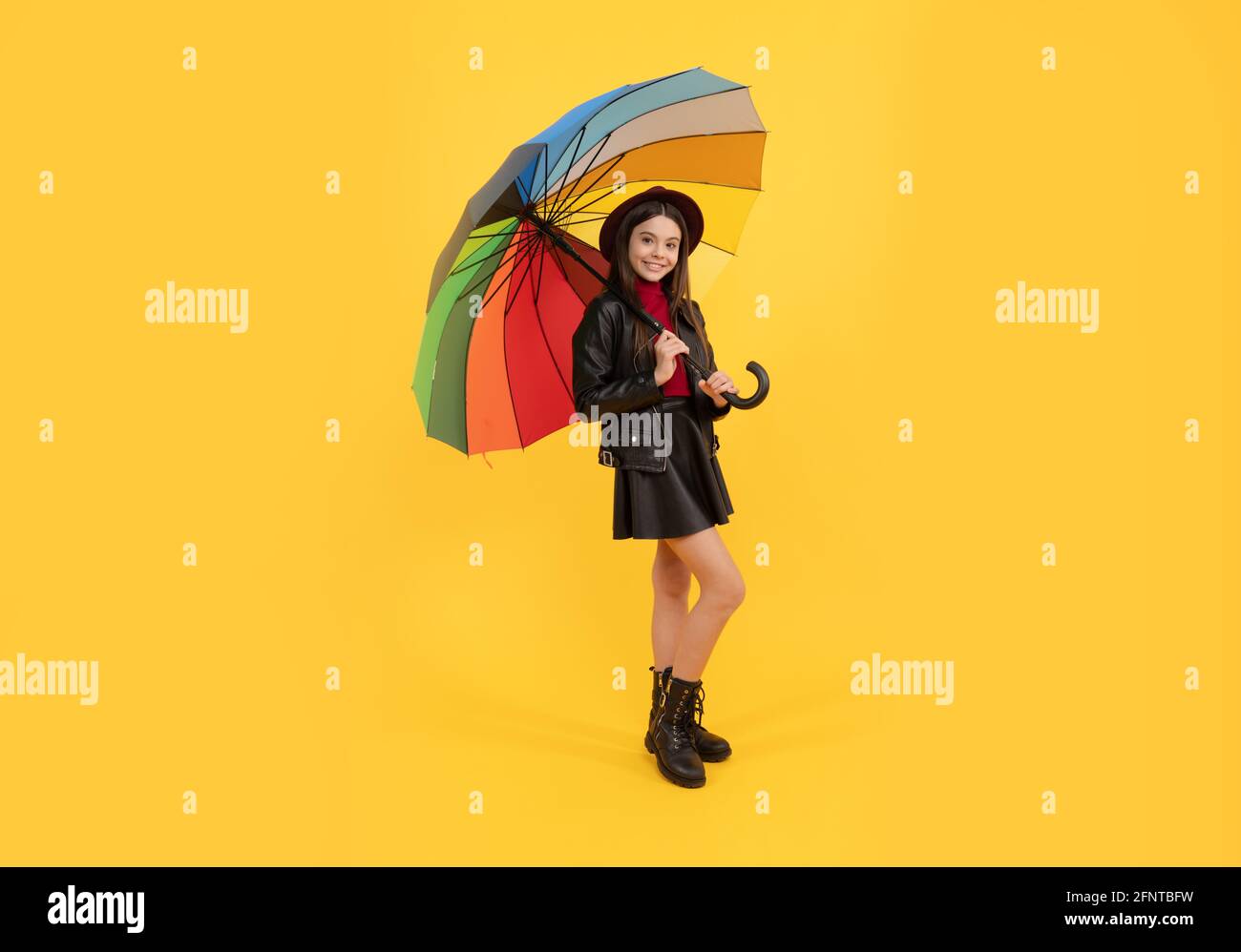 felice ragazza teen in cappello e vestiti di pelle sotto ombrello arcobaleno, tempo di autunno Foto Stock