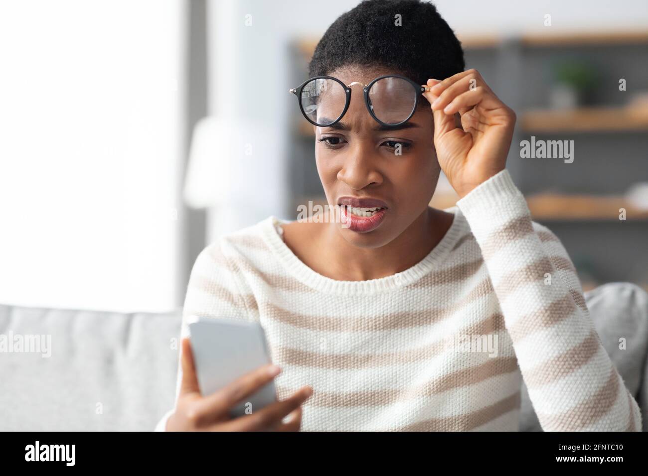 Messaggio errato. African Female sconvolto che decolta gli occhiali e guarda lo schermo dello smartphone Foto Stock