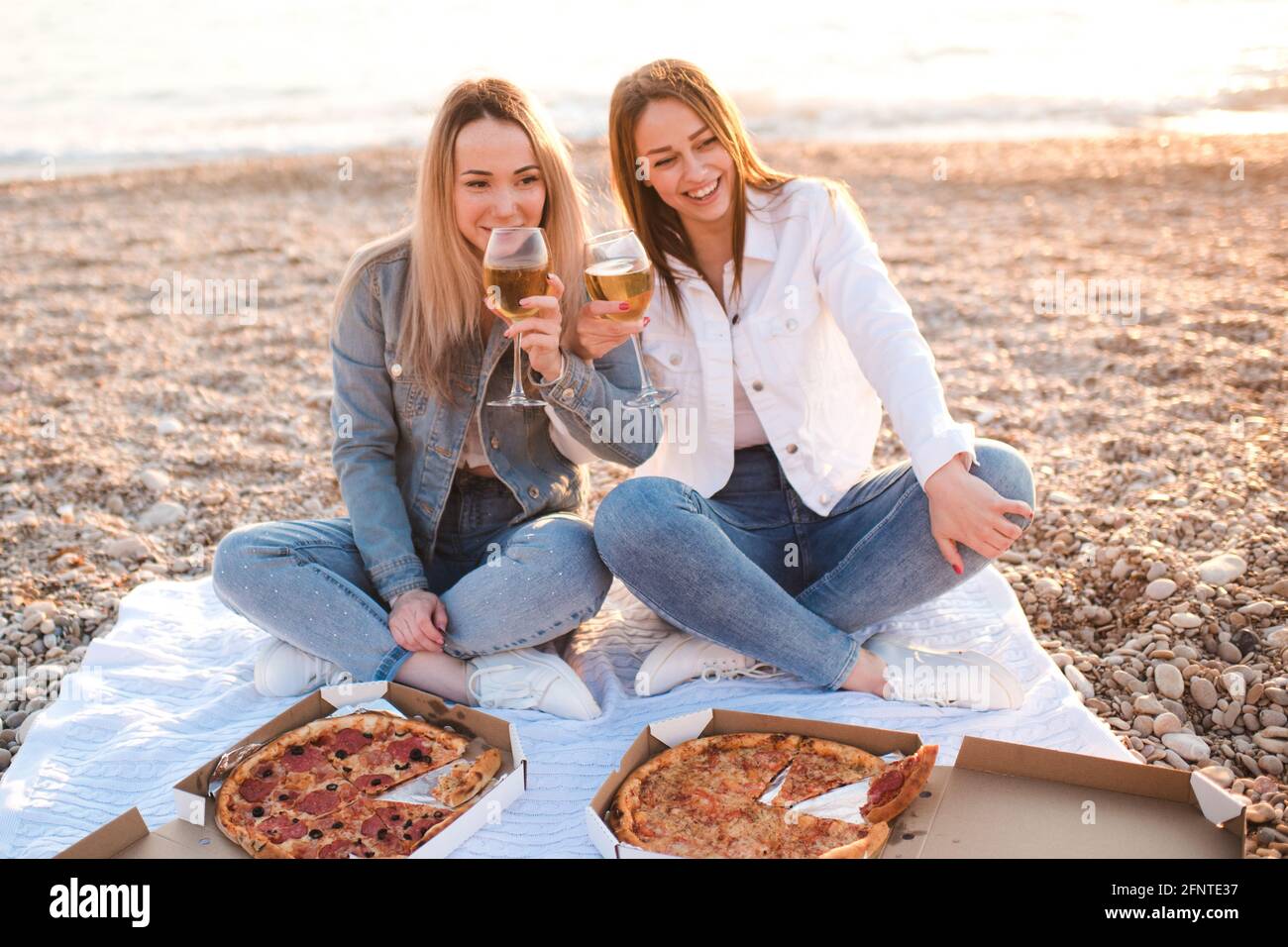 Due giovani belle fidanzate divertirsi con pizza e vino in spiaggia sulla riva del mare all'aperto sotto la luce del sole. Stagione estiva. Amicizia. Foto Stock