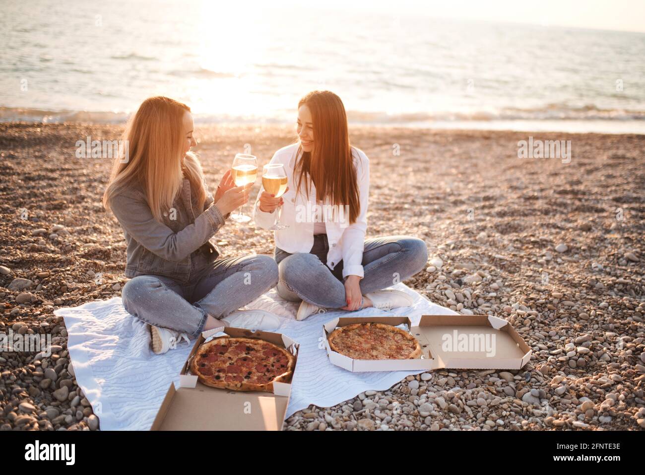 Due giovani belle fidanzate divertirsi con pizza e vino in spiaggia sulla riva del mare all'aperto sotto la luce del sole. Stagione estiva. Amicizia. Foto Stock