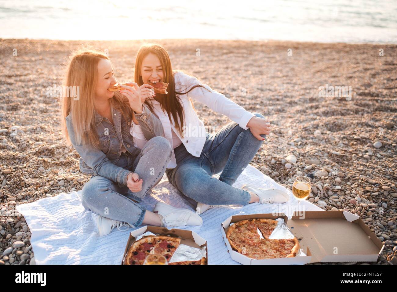 Due giovani belle fidanzate divertirsi con pizza e vino in spiaggia sulla riva del mare all'aperto sotto la luce del sole. Stagione estiva. Amicizia. Foto Stock