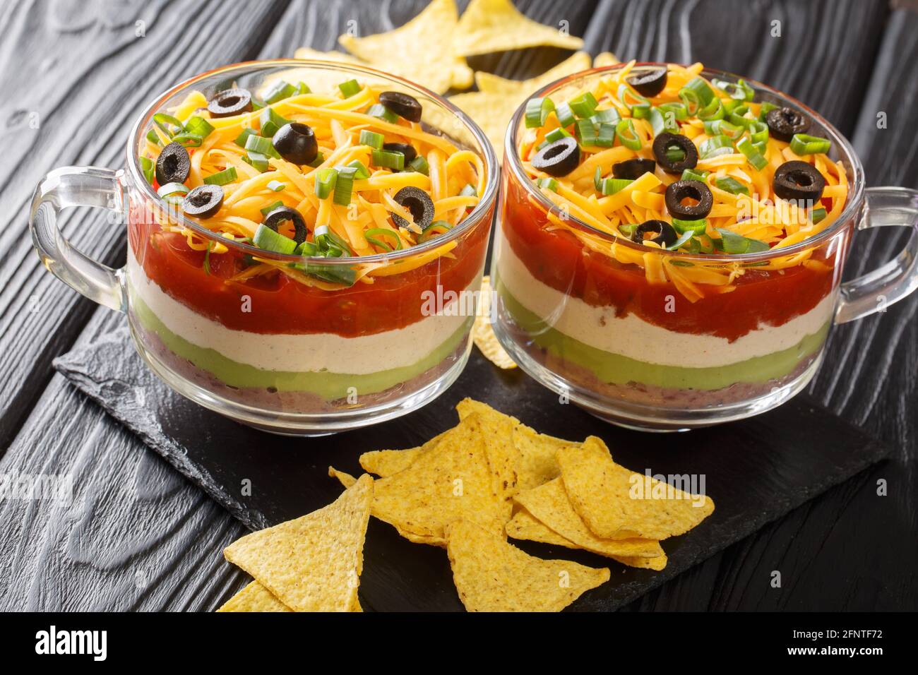 Delizioso antipasto cibo messicano a sette strati insalata di immersione servita con patatine primo piano sul tavolo. Orizzontale Foto Stock