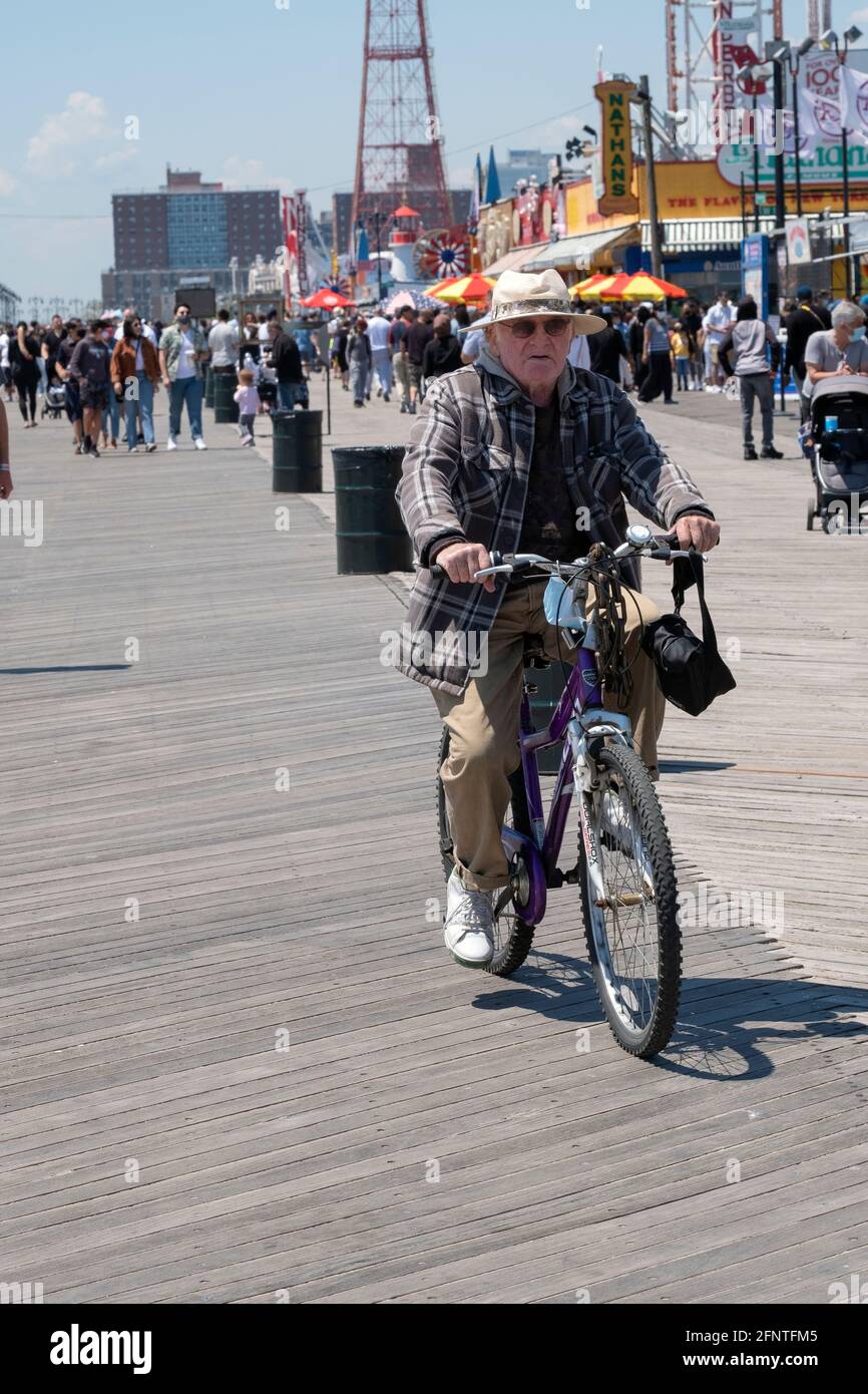 Un uomo più anziano che indossa un ampio cappello a forma di brimmetto fa un giro in bicicletta sul lungomare di Coney Island, Brooklyn, New York City. Foto Stock