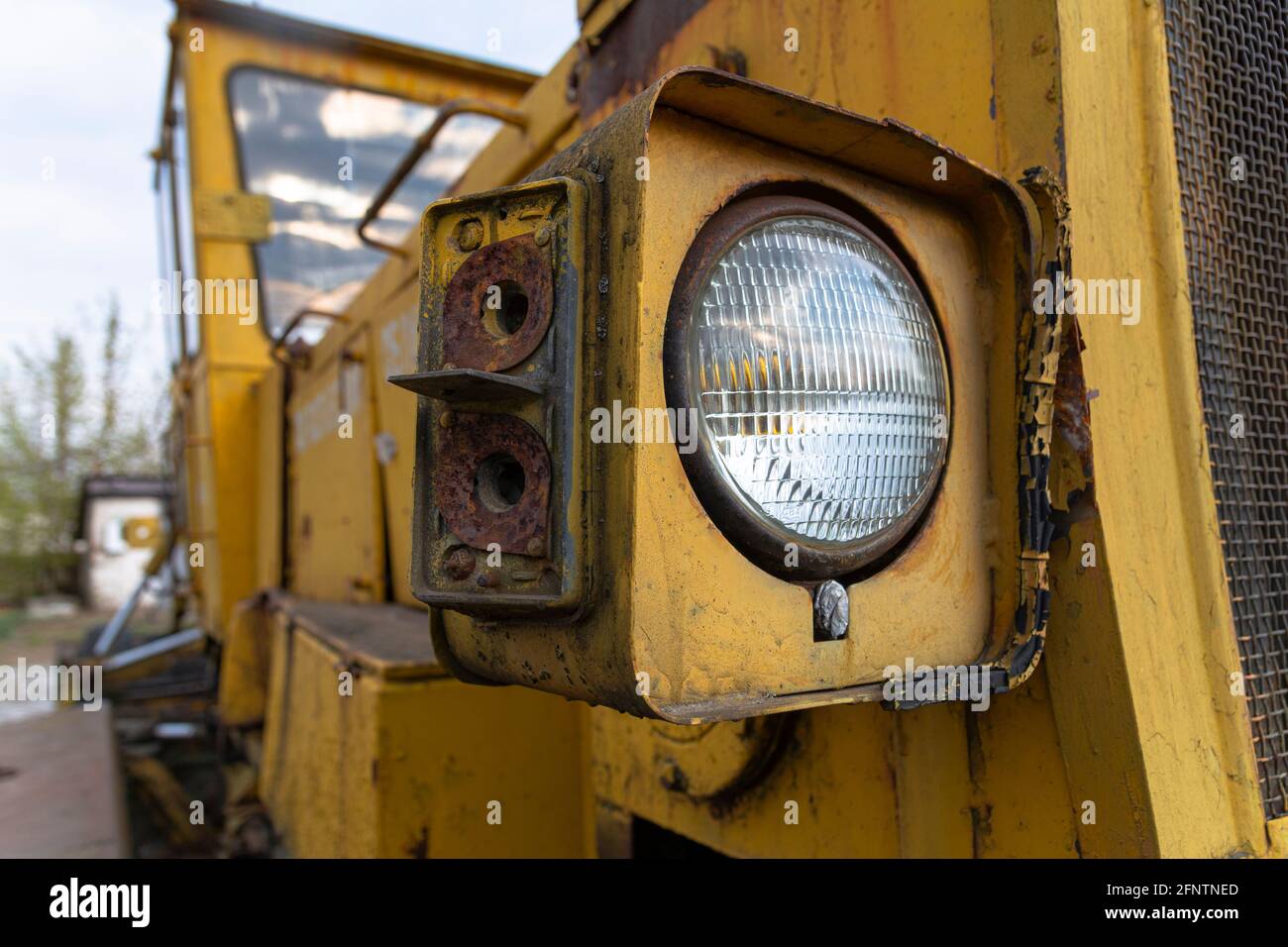 Faro di una vecchia macchina abbandonata per la costruzione di strade rotte (livellatrice). Metallo arrugginito, vetro rotto e resti di vernice vecchia. Foto Stock