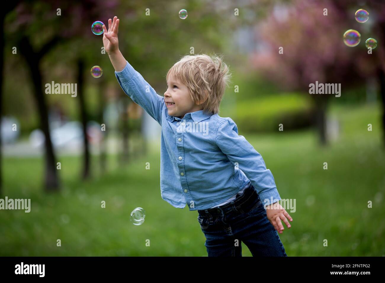 Bambino biondo, ragazzo carino in abbigliamento casual, giocando con bolle  di sapone nel parco, correre felicemente Foto stock - Alamy