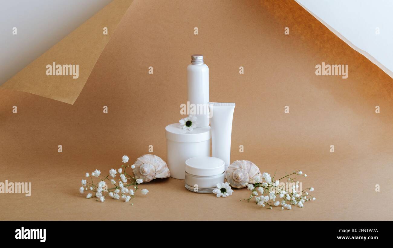 Set prodotti cosmetici per la cura della pelle di bellezza naturale con conchiglie di mare fiori su sfondo marrone beige. Kit bianco tubo crema prodotti cosmetici per il corpo Foto Stock