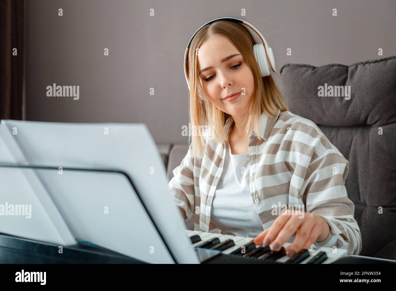 Donna in cuffia che suona musica piano su sintetizzatore da note. Teenager ragazza musicista pianista migliora le capacità di suonare piano. Hobby dell'educazione musicale Foto Stock