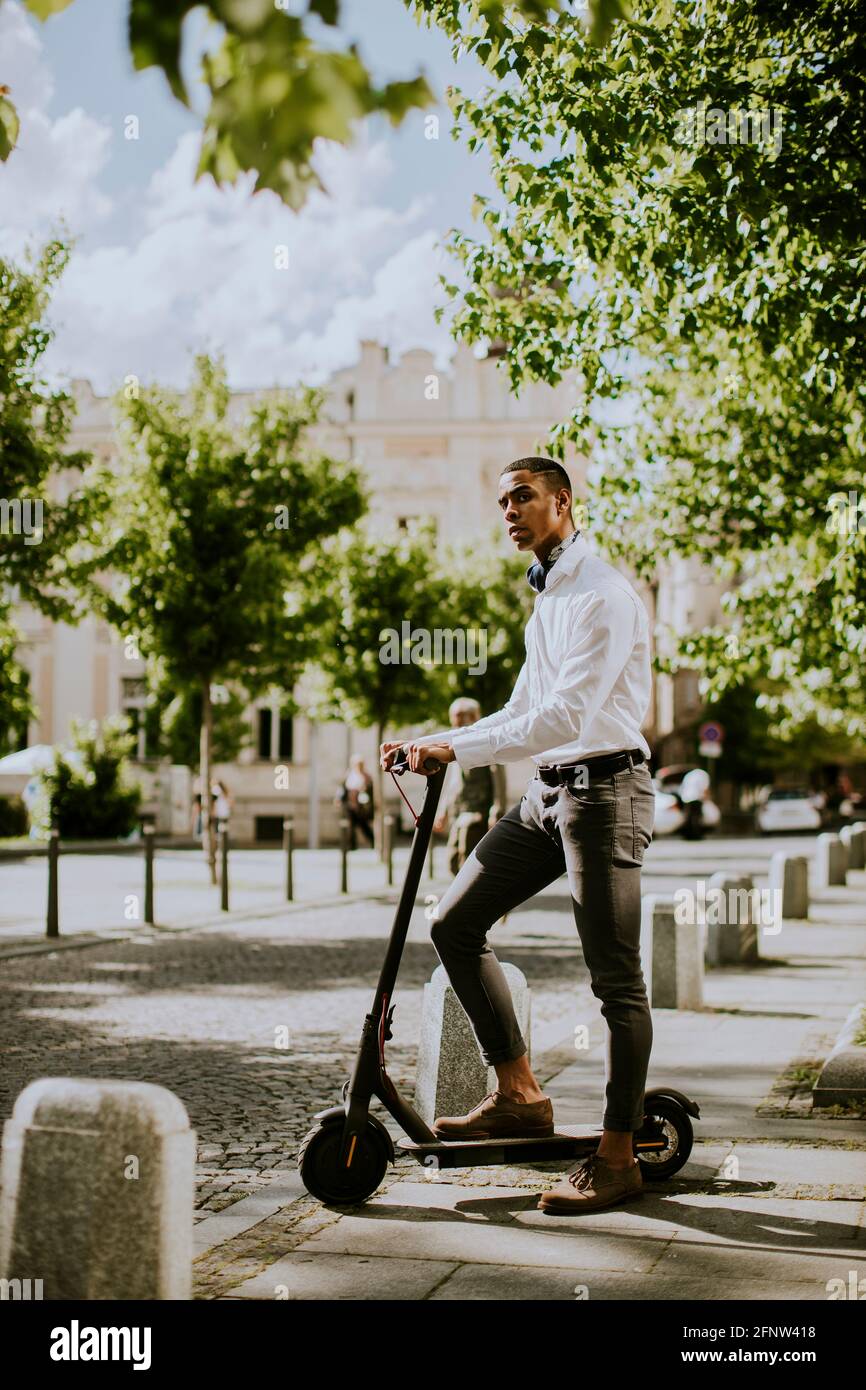 Bel giovane afroamericano con scooter elettrico su una strada Foto Stock