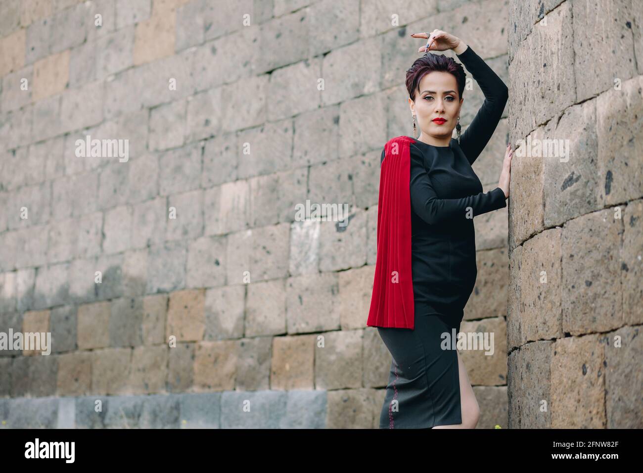 Foto media di bella e attraente donna con mantello rosso in posa accanto all'antico castello Foto Stock
