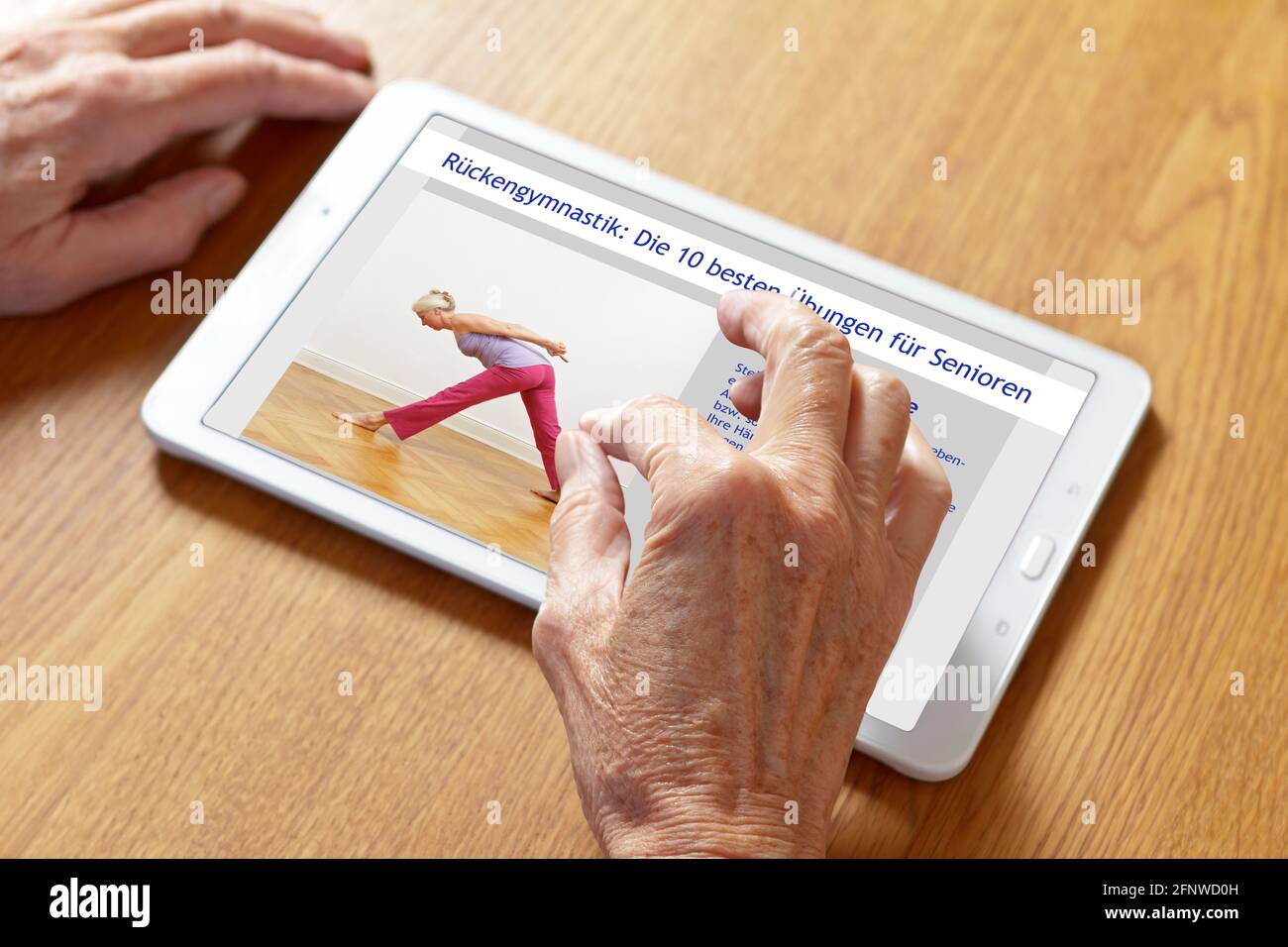 Mani di una donna anziana che zoomano sulle istruzioni tedesche su un PC tablet, traduzione di testo: I 10 migliori esercizi schiena per anziani. Foto Stock