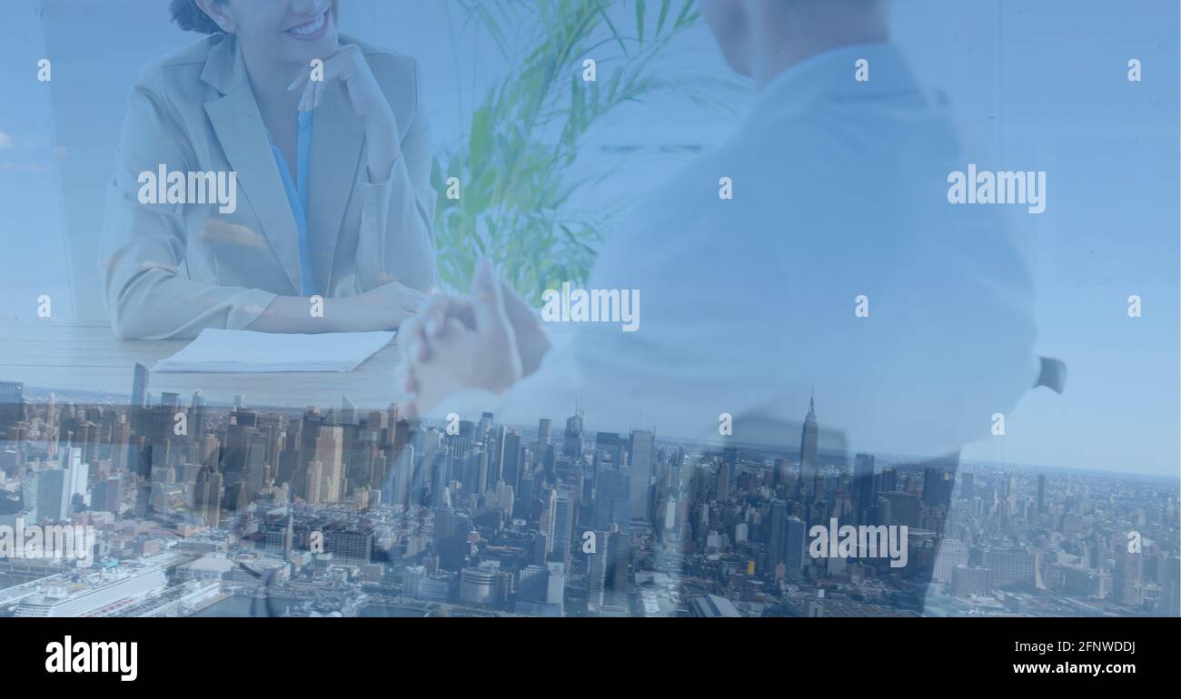 Composizione della sezione centrale dell'uomo d'affari e della donna d'affari sorridente in riunione sopra il paesaggio urbano moderno Foto Stock