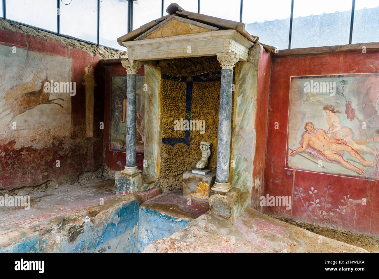 Biclinium (sala da pranzo) - Casa di Ottavio quartiere - Pompei sito archeologico, Italia Fontana centrale che scorre da una struttura in stile tempio supportata da due colonne corinzie. Affreschi, uno su entrambi i lati della fontana. I soggetti di entrambi gli affreschi - Narciso in primavera (a sinistra) e Piramo che si suicidano (a destra) - condividono un tema comune: La morte portata avanti dalla passione. Foto Stock