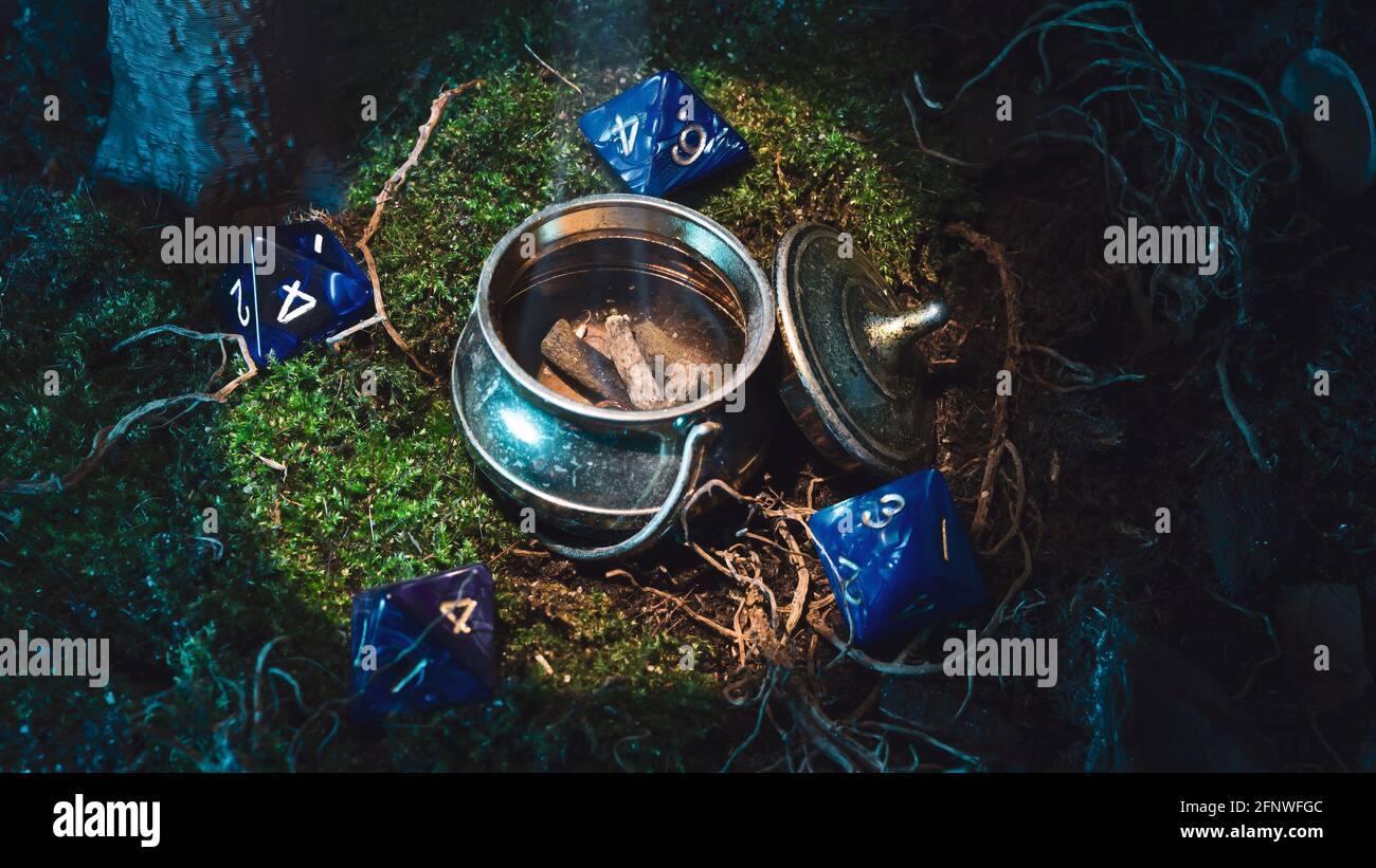 Scena di gioco di ruolo di un bollitore metallico in miniatura circondato da dadi a 8 lati su muschio verde Foto Stock